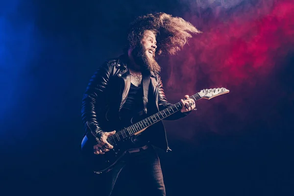 Expresszív férfi rock gitáros hosszú hajjal és szakállal játszik a füst háttér. Stúdió felvétel — Stock Fotó