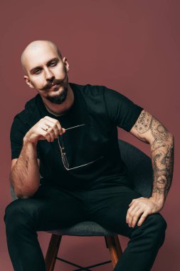 Bıyıklı yakışıklı sakallı adamın stüdyoda sandalyede otururken elinde gözlük tuttuğunu düşünsene. 