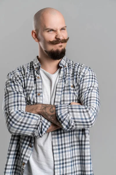 Homem barbudo careca com bigode isolado em fundo cinza cruzou os braços parecendo cético de lado — Fotografia de Stock