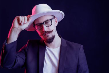 Beyaz kenarlı şapkalı, ceketli, gözlüklü, kameraya bakan hippi sakallı adam. Renk filtreleri