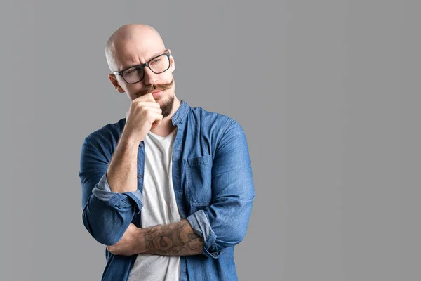 Porträt eines denkenden Mannes mit Glatze und Brille, der die Faust aufs Kinn hält, isoliert auf grauem Hintergrund — Stockfoto