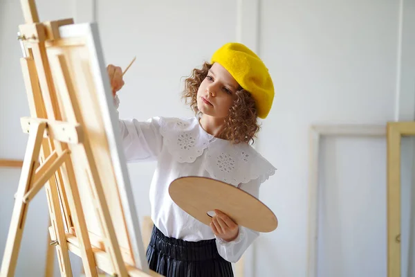 Retrato de pequeno artista em boina amarela que pinta imagem em estúdio, enquanto mantém a cor pallete — Fotografia de Stock