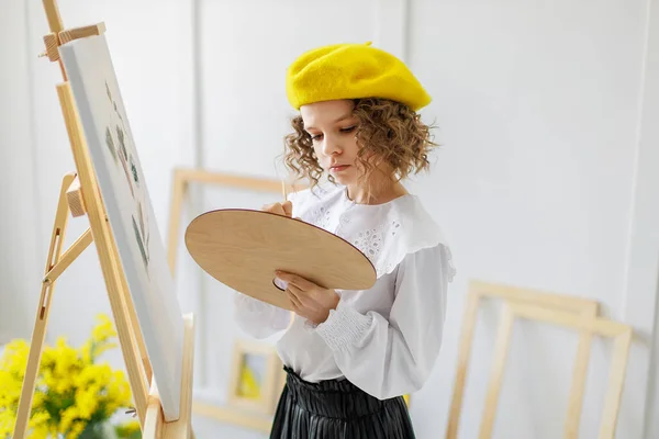 Portrait of little girl artist in yellow beret who paints picture in studio while holds pallete — Stock Photo, Image