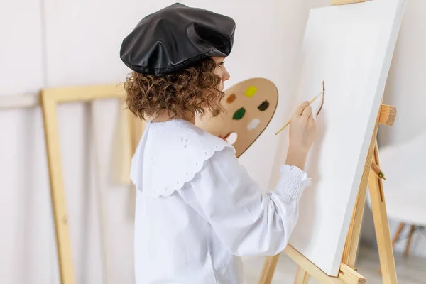 Menina pintando um quadro em um estúdio ou escola de arte. Criança pintor criativo e pensativo pinta um quadro colorido em tela na oficina. Crianças talentosas — Fotografia de Stock