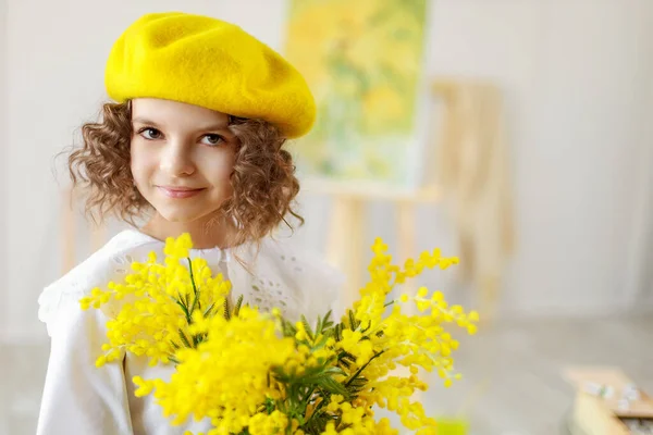 Ritratto di una piccola graziosa ragazza riccia in berretto giallo e collant che posa in studio mentre tiene in mano fiori gialli — Foto Stock