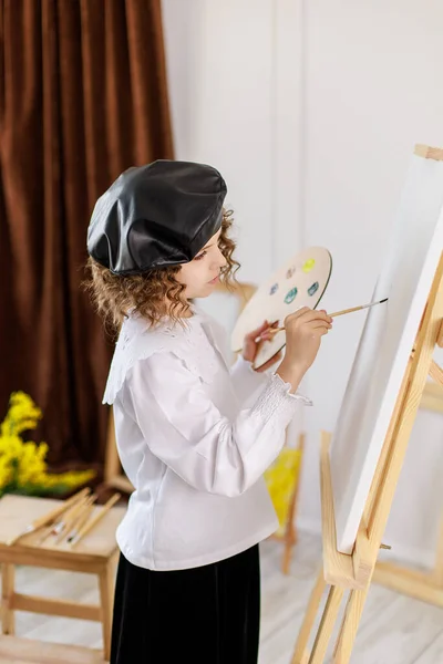 Menina pintando um quadro em um estúdio ou escola de arte. Criança pintor criativo e pensativo pinta um quadro colorido em tela na oficina. Crianças talentosas — Fotografia de Stock