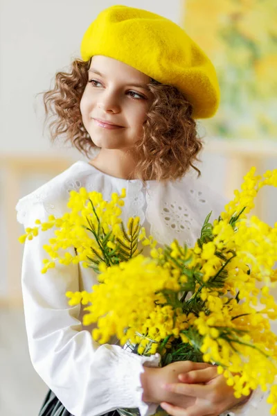 Portré egy kis aranyos göndör lány sárga svájcisapka és harisnya, aki pózol a stúdióban, miközben a kezében sárga virágok — Stock Fotó