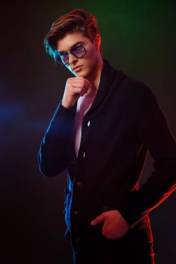 Neon ışıklı, orta boylu, siyah saçlı, güneş gözlüğü takan yakışıklı erkek modelin portresi.