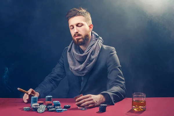 A wealthy mature man drinking brandy and playing poker with the excitement in a casino.