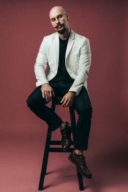 Kameraya bakarken sandalyede oturan genç bir iş adamının tüm vücudu.