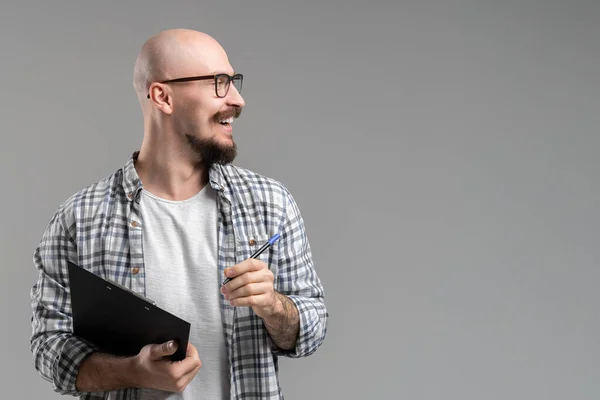 Handsome balded beard with musctache man wearing casual clothes holding clipboard smiling isolated over gray background. — Stockfoto