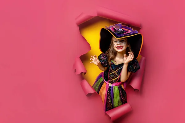 Tertawa lucu gadis kecil dalam kostum penyihir halloween mencari, tersenyum dan takut melalui lubang merah, kertas kuning latar belakang. Ruang penyalinan — Stok Foto