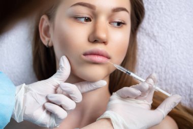 Çekici genç bir kadın canlandırıcı yüz enjeksiyonu yaptırıyor. O, klinikte sakince oturuyor. Uzman güzellik uzmanı hyaluronik asitle kadın kırışıklıklarını dolduruyor.. 