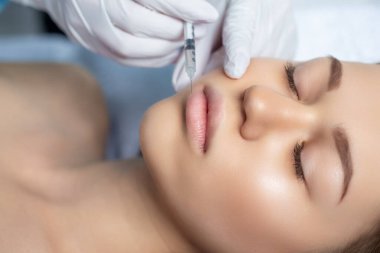 Çekici genç bir kadın canlandırıcı yüz enjeksiyonu yaptırıyor. O, klinikte sakince oturuyor. Uzman güzellik uzmanı hyaluronik asitle kadın kırışıklıklarını dolduruyor.. 