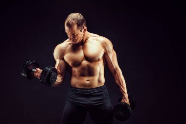 Egzersizleri halterlerle yapan güçlü bir adam. Siyah arka planda izole edilmiş iyi fizikli genç bir adamın fotoğrafı. Kuvvet ve motivasyon. 