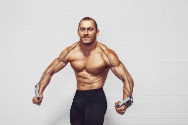 Yakışıklı genç sporcu beyaz arka planda dururken genişletici kullanarak egzersiz yapıyor. Stüdyo çekimi. Sağlıklı spor konsepti 