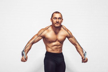 Yakışıklı genç sporcu beyaz arka planda dururken genişletici kullanarak egzersiz yapıyor. Stüdyo çekimi. Sağlıklı spor konsepti 