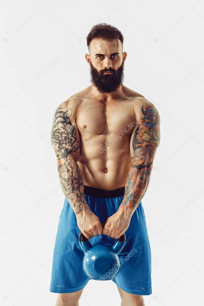 Muscular shirtless tattooed bearded male athlete bodybuilder workout with kettlebell on a white background. Isolate. 