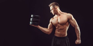 Güç, güç, mükemmel vücut geliştirme, spor konsepti. Genç yakışıklı kaslı adam mükemmel vücut gösteriyor ve siyah balmumunda peynir halkaları tutuyor.. 