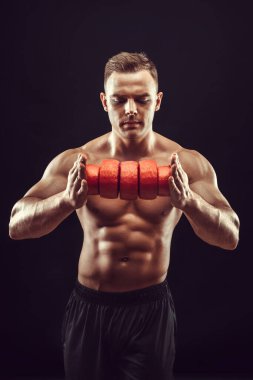 Güç, güç, mükemmel vücut geliştirme, spor konsepti. Genç yakışıklı kaslı adam mükemmel vücut gösteriyor ve turuncu balmumunda peynir çemberleri tutuyor.. 