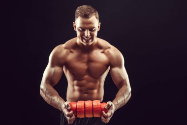 Güç, güç, mükemmel vücut geliştirme, spor konsepti. Genç yakışıklı kaslı adam mükemmel vücut gösteriyor ve turuncu balmumunda peynir çemberleri tutuyor.. 