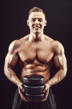 Güç, güç, mükemmel vücut geliştirme, spor konsepti. Genç yakışıklı kaslı adam mükemmel vücut gösteriyor ve siyah balmumunda peynir halkaları tutuyor.. 
