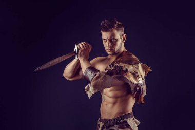 Portrait of handsome muscular gladiator with sword. Isolated. Studio shot. Dark background. 