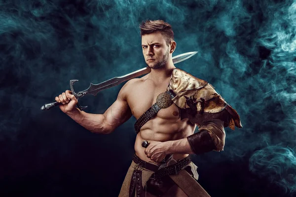 Portrait of handsome muscular gladiator with sword. Isolated. Studio shot. Dark background. 