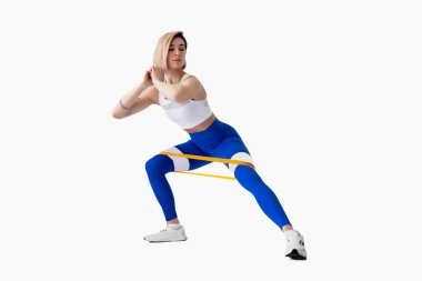 Spor giyimli seksi kadın egzersiz rutininde direniş bandı kullanıyor. Genç bir kadın beyaz arka planda spor yapıyor. İzole et. 