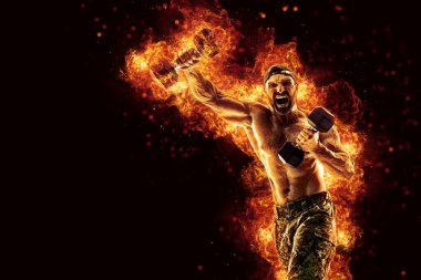 Handsome bearded shirtless tattooed bodybuilder workout wih dumbbell like boxer. Fire art concept. 