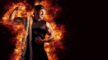 Muscular man working out with battle ropes. Flame background. 