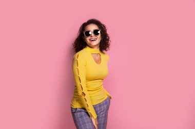 Beautiful young curly caucasian girl in a yellow outfit , who is smiling and posing on pink background.