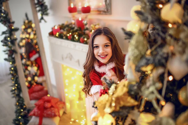 クリスマスと新年 暖かい黄色のセーターを着た幸せな女の子は 喜びの笑顔でクリスマスツリーの後ろから顔をのぞかせます お正月とクリスマスおめでとう — ストック写真