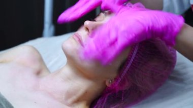 Hoş bir masaj yaptırırken dinlenen genç bir kadın, nazikçe yüz, omuz ve boyun masajı yapan bir terapist..