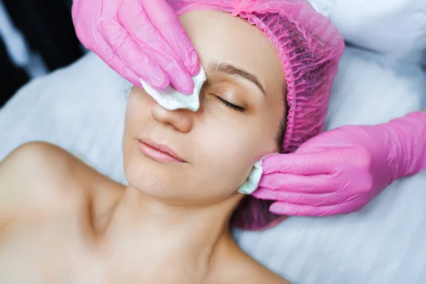 Cosmetologist applies cream on the skin of the client.