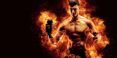 Protein içeceğiyle kaslı bir adam karanlık arka planda ateş alevleriyle sallanıyor..