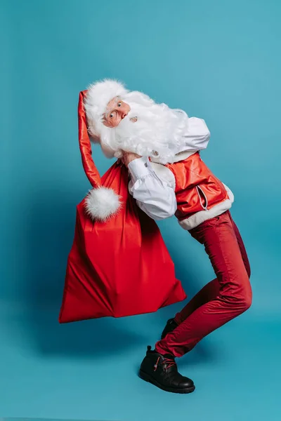 全身上下都是快乐的圣诞老人 他带着一个大袋子 里面的玩具与彩色工作室的背景格格不入 — 图库照片
