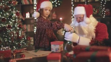 Noel Baba ve küçük asistan kız çocuklar için Noel hediyesi paketliyorlar. YILI YIL KONUŞMASI.