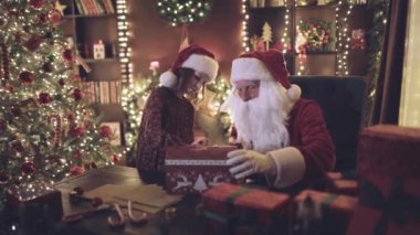 Noel Baba, masadaki Noel ağacının yanında otururken yardımcısına sihirli bir kutuyla sürpriz yapıyor. Kız Noel Baba 'ya sarılıyor. Yeni yıl konsepti. 