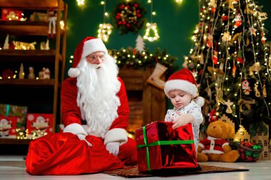 Küçük çocuk Noel ağacının yanında Noel Baba 'dan büyük bir Noel hediyesi alıyor. Noel Sahneleri. Yeni yıl konsepti 