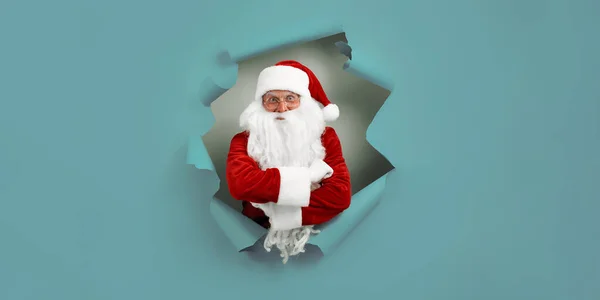 Santa Clause peeking through a paper hole while crossing hands. christmas advertisement concept. New Year concept