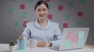 Asyalı bir kadının ev bilgisayarında çalışırken kafası karışıyor ve kameraya bakıyor..