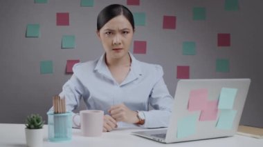 Asyalı bir kadın laptopta çalışırken kafasını kaşıyarak kafasını karıştırır..