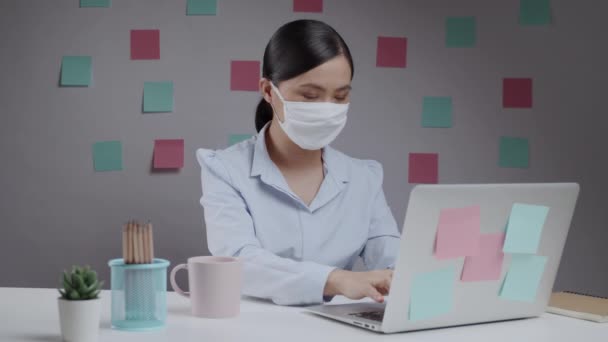 在总部的笔记本电脑上工作的亚洲女人戴着防护面罩 — 图库视频影像