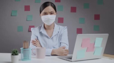 Asyalı kadın koruyucu yüz maskesi takıyor. Ev ofisinde el işareti yapıyor..