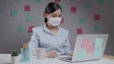 Maske takan Asyalı kadın ev ofisteki bilgisayarla görüntülü görüşme yapmaktan memnun..