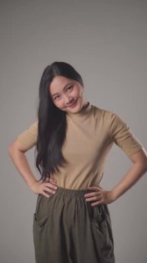 Kendine güvenen Asyalı kadın gülümseyerek ayakta duruyor ve arka planda tek başına kameraya bakıyor. 4K video.