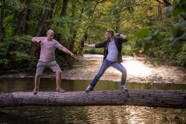 İki adam, kütük bir köprüde dövüş sanatları stiliyle komik bir şekilde dövüşüyor.