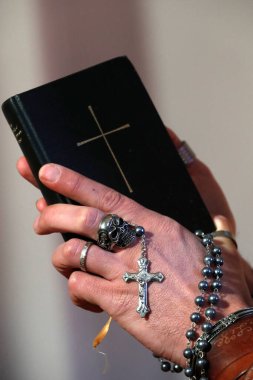 Kafatası yüzüklü bir adam tespih çekiyor ve İncil okuyor. Yakın plan. Fransa.