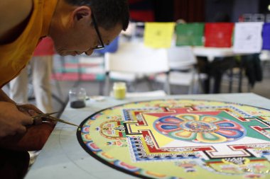 Tibetli keşiş renkli bir Kum Mandala üzerinde dikkatle çalışıyor. 